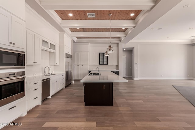 kitchen featuring sink, hanging light fixtures, built in appliances, a center island with sink, and beamed ceiling