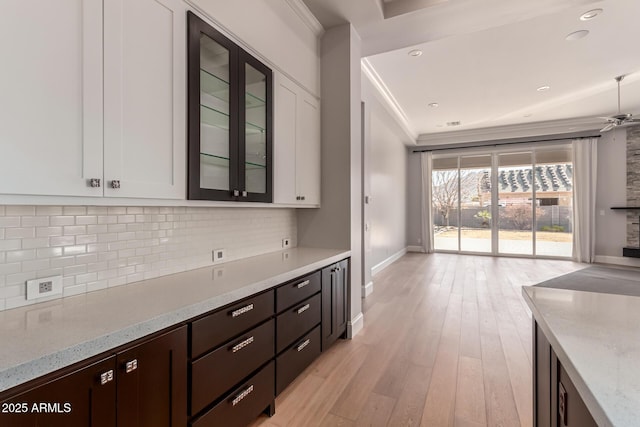 kitchen with white cabinetry, backsplash, ornamental molding, light stone counters, and light hardwood / wood-style flooring