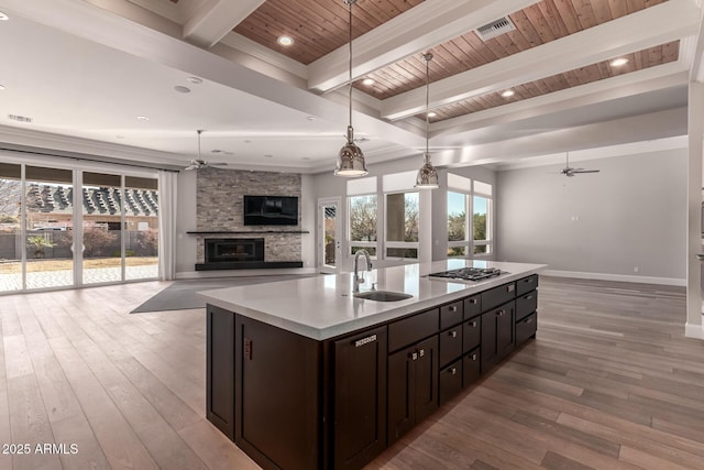 kitchen featuring a stone fireplace, sink, decorative light fixtures, an island with sink, and ceiling fan