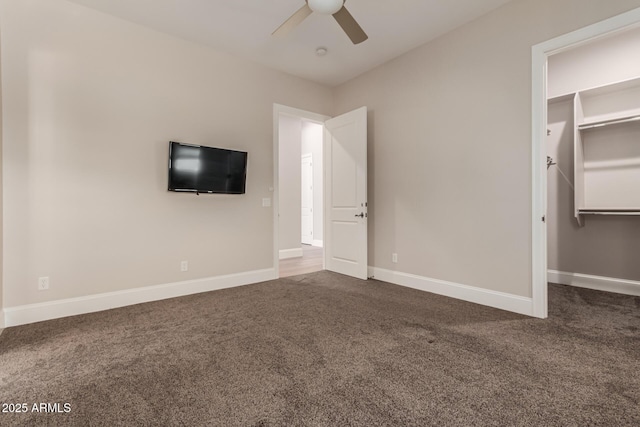 unfurnished bedroom featuring dark carpet, ceiling fan, and a spacious closet