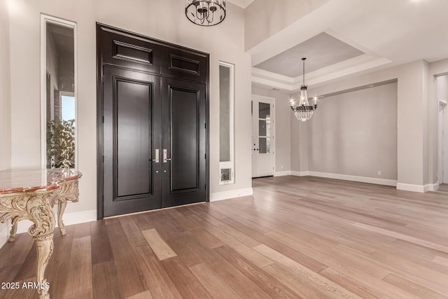 foyer entrance featuring an inviting chandelier, a tray ceiling, light hardwood / wood-style flooring, and french doors