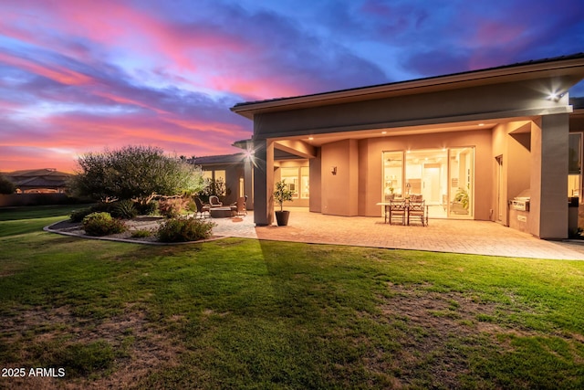 back house at dusk featuring a yard and a patio