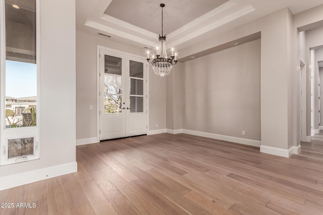 unfurnished dining area with hardwood / wood-style flooring, a notable chandelier, and a tray ceiling