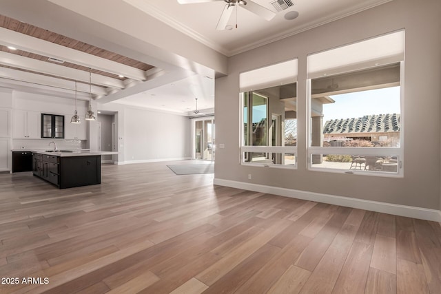 unfurnished living room with sink, ceiling fan, light hardwood / wood-style floors, crown molding, and beam ceiling