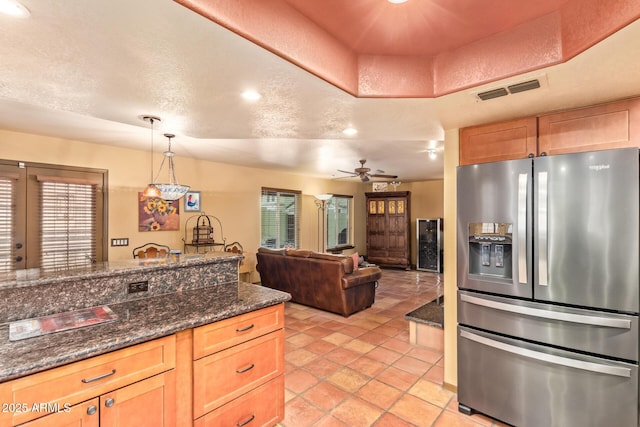 kitchen with visible vents, light brown cabinets, decorative light fixtures, a textured ceiling, and stainless steel fridge