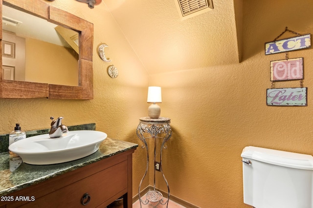 half bathroom with visible vents, toilet, vanity, and a textured wall