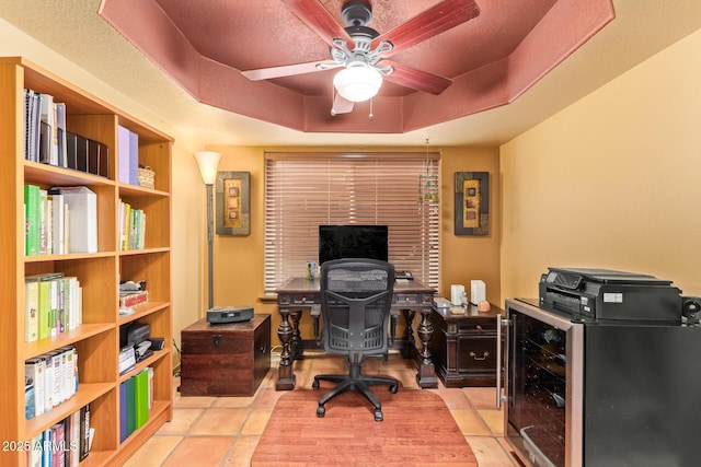 home office featuring tile patterned floors, ceiling fan, beverage cooler, and a tray ceiling