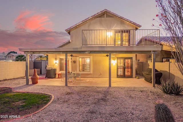 back of property at dusk with a patio, fence, stucco siding, ceiling fan, and french doors