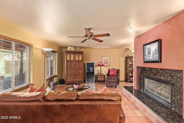 living area featuring light tile patterned floors, a fireplace, arched walkways, ceiling fan, and a textured ceiling