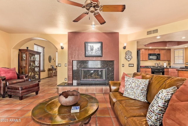 living area with light tile patterned floors, a ceiling fan, visible vents, arched walkways, and a tile fireplace