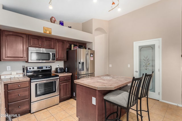 kitchen featuring light tile patterned floors, a kitchen breakfast bar, tile countertops, a kitchen island, and appliances with stainless steel finishes