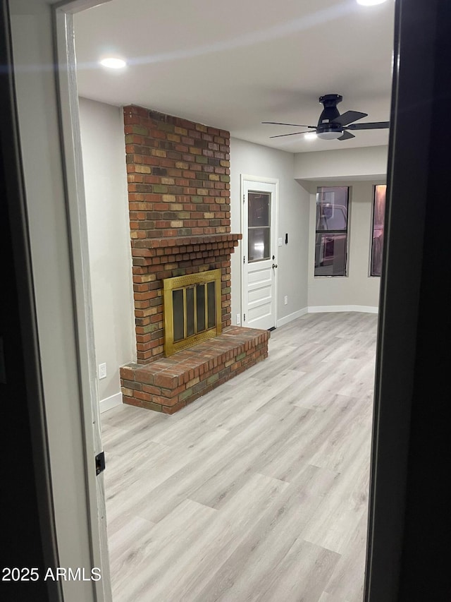 unfurnished living room with a fireplace, wood finished floors, baseboards, and ceiling fan