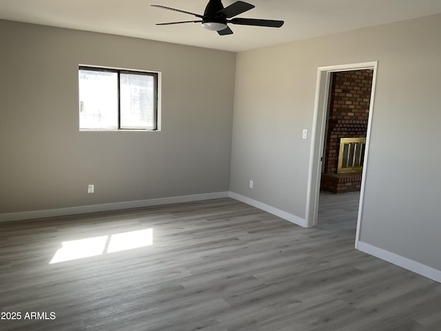 spare room with a fireplace, wood finished floors, a ceiling fan, and baseboards