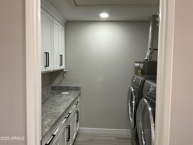 clothes washing area featuring washer and dryer, water heater, cabinet space, light wood-style floors, and baseboards