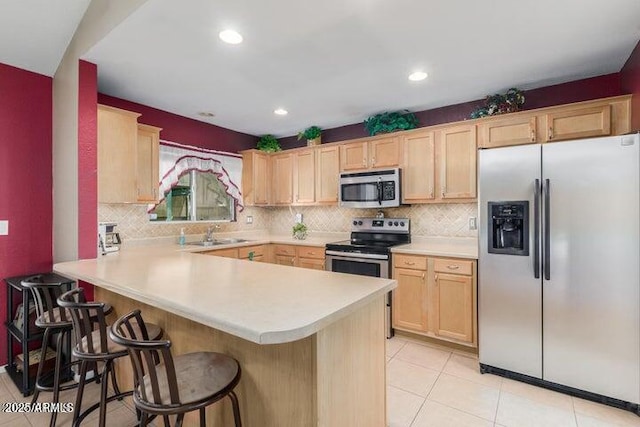 kitchen with light brown cabinetry, stainless steel appliances, and kitchen peninsula