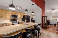 kitchen with pendant lighting, a breakfast bar area, appliances with stainless steel finishes, light tile patterned flooring, and light brown cabinetry