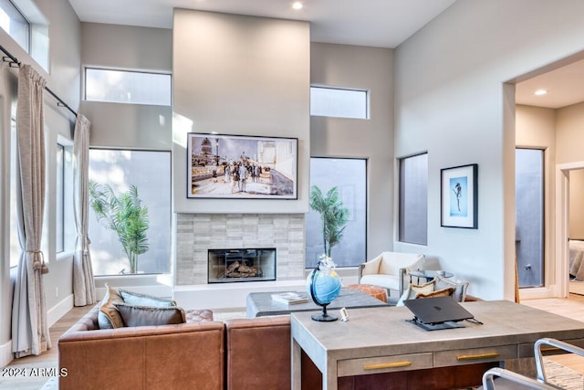 living room with a towering ceiling, light hardwood / wood-style floors, and a tiled fireplace