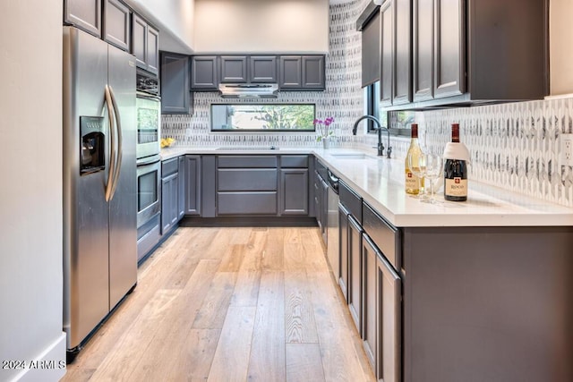 kitchen with gray cabinetry, backsplash, sink, light wood-type flooring, and appliances with stainless steel finishes