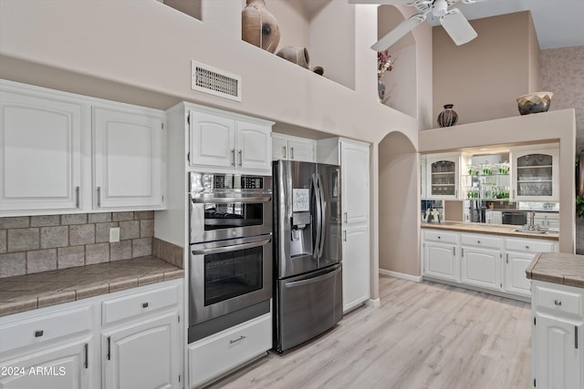 kitchen featuring tile countertops, white cabinetry, appliances with stainless steel finishes, a towering ceiling, and tasteful backsplash