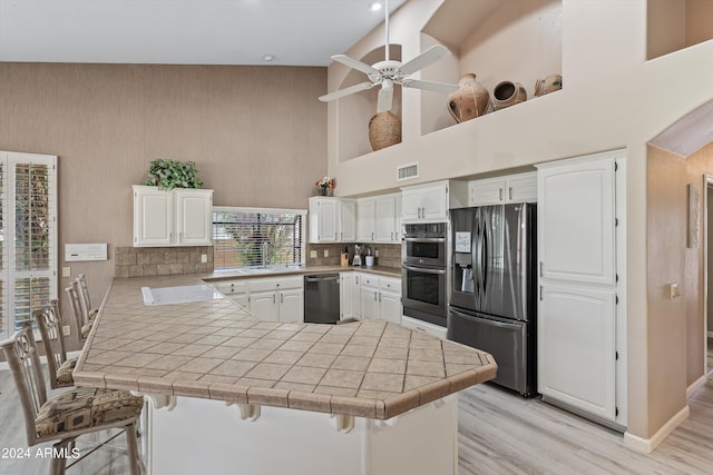 kitchen with kitchen peninsula, white cabinets, a breakfast bar area, appliances with stainless steel finishes, and high vaulted ceiling