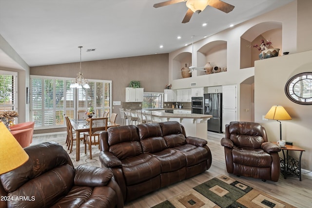 living room with light hardwood / wood-style flooring, high vaulted ceiling, and ceiling fan with notable chandelier