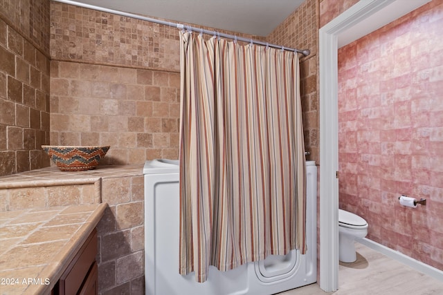 bathroom with toilet, a shower with shower curtain, vanity, and tile walls