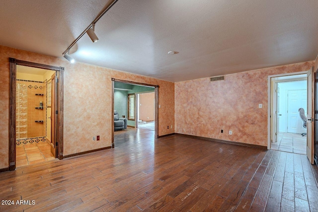 empty room featuring hardwood / wood-style floors, rail lighting, and a textured ceiling