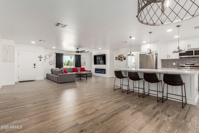 kitchen with visible vents, decorative backsplash, a glass covered fireplace, appliances with stainless steel finishes, and light countertops