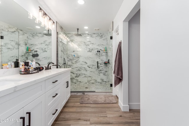 full bath with a marble finish shower, double vanity, recessed lighting, a sink, and wood finished floors