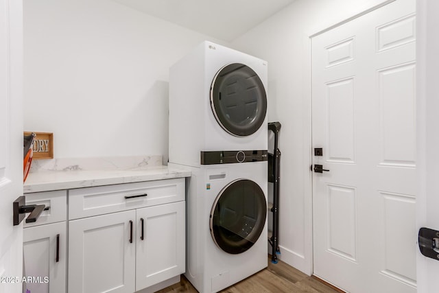 laundry room with stacked washer and dryer, light wood-style flooring, and cabinet space