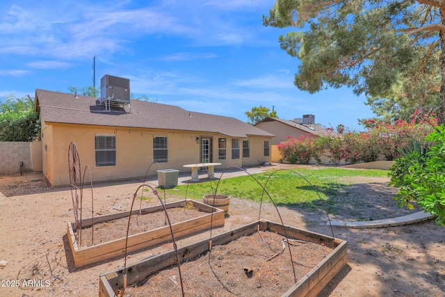 back of house featuring fence, central AC unit, stucco siding, and a vegetable garden