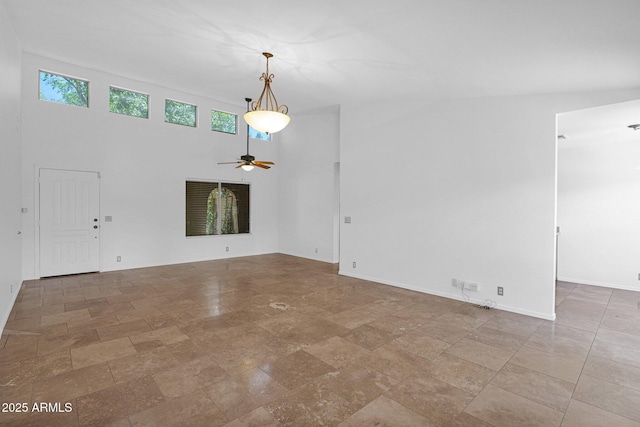 empty room featuring baseboards, ceiling fan, stone finish flooring, and a towering ceiling