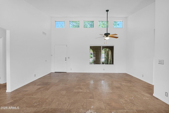 unfurnished living room featuring baseboards, a high ceiling, stone finish floor, and a ceiling fan