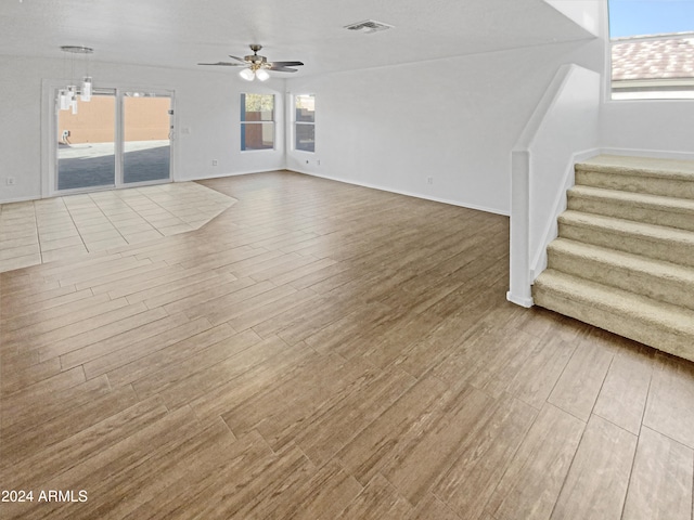 unfurnished living room featuring ceiling fan with notable chandelier and light hardwood / wood-style floors