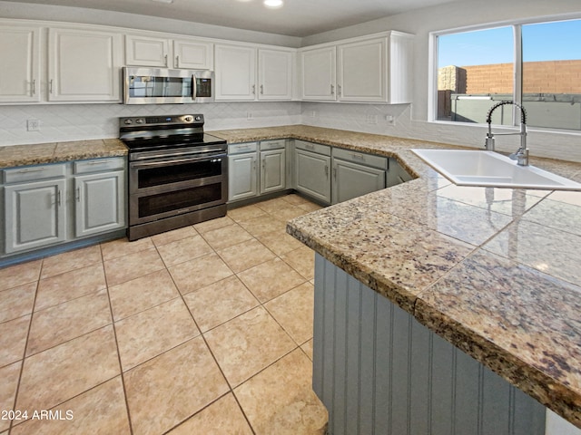 kitchen with gray cabinetry, white cabinets, sink, light tile patterned flooring, and stainless steel appliances