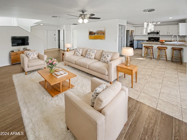 living room featuring sink, ceiling fan with notable chandelier, and light wood-type flooring