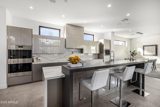 kitchen featuring a kitchen island with sink, stainless steel double oven, a breakfast bar, and decorative light fixtures