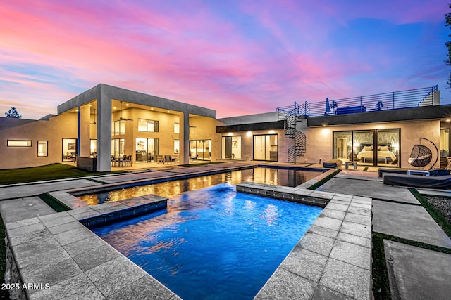 pool at dusk featuring a patio area and an in ground hot tub