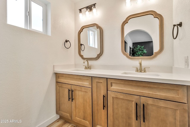 full bath with double vanity, wood finished floors, baseboards, and a sink