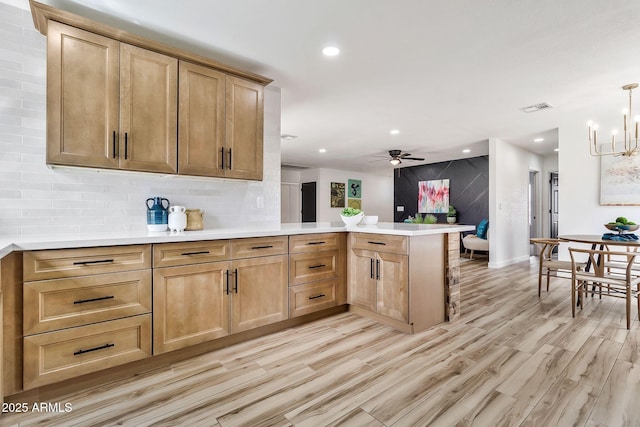 kitchen featuring tasteful backsplash, visible vents, ceiling fan with notable chandelier, a peninsula, and light wood-style floors