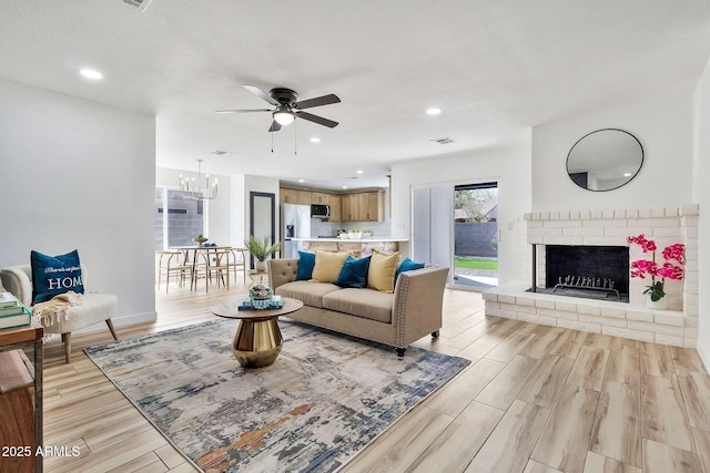 living area with light wood finished floors, visible vents, a brick fireplace, ceiling fan with notable chandelier, and recessed lighting