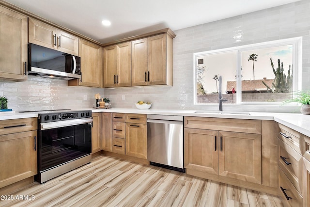 kitchen with a sink, backsplash, appliances with stainless steel finishes, and light countertops