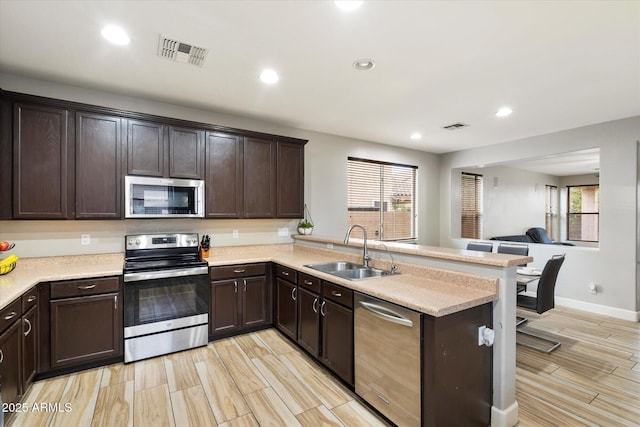 kitchen featuring stainless steel appliances, sink, dark brown cabinetry, and kitchen peninsula