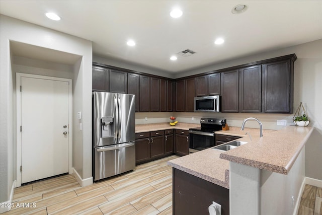 kitchen with appliances with stainless steel finishes, kitchen peninsula, sink, and dark brown cabinets