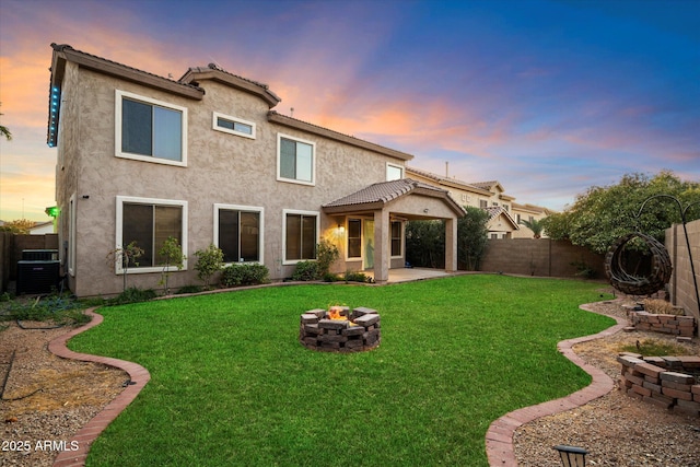 back house at dusk with a patio area, a lawn, central air condition unit, and an outdoor fire pit