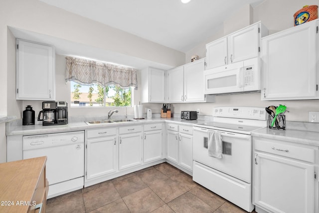 kitchen with white appliances, sink, vaulted ceiling, light tile patterned floors, and white cabinetry