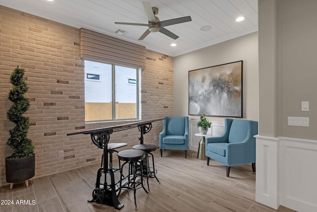 sitting room featuring visible vents, a wainscoted wall, brick wall, crown molding, and light wood-style floors