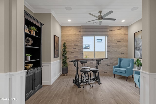 interior space with brick wall, light wood-style flooring, ornamental molding, and wainscoting