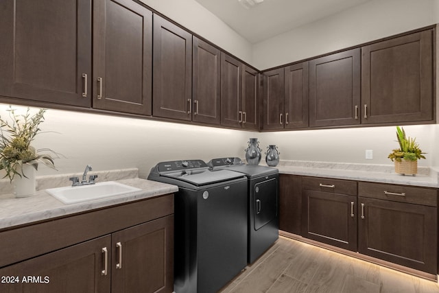 laundry area with light wood-type flooring, cabinet space, washing machine and dryer, and a sink