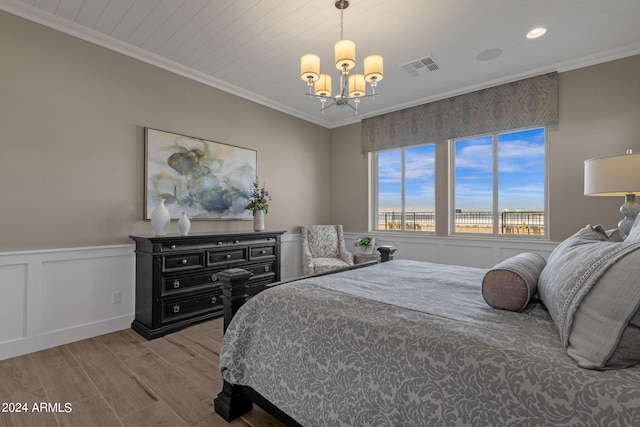 bedroom featuring a wainscoted wall, a decorative wall, ornamental molding, wood finished floors, and a chandelier